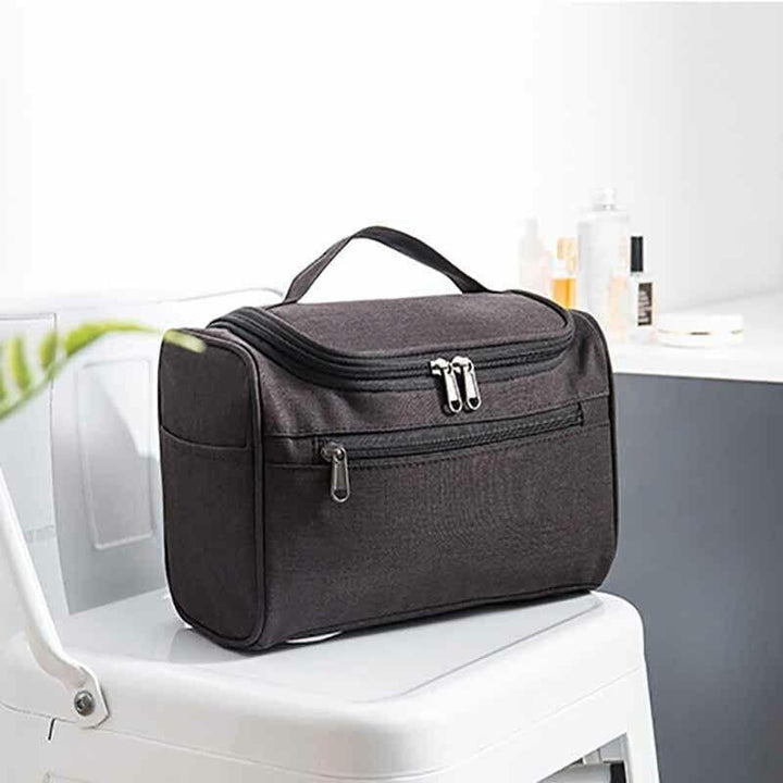 Borsa da toilette nera su sedia bianca, con zip multiple, ideale per viaggi. Design compatto, resistente all'acqua, perfetta per organizzare accessori.