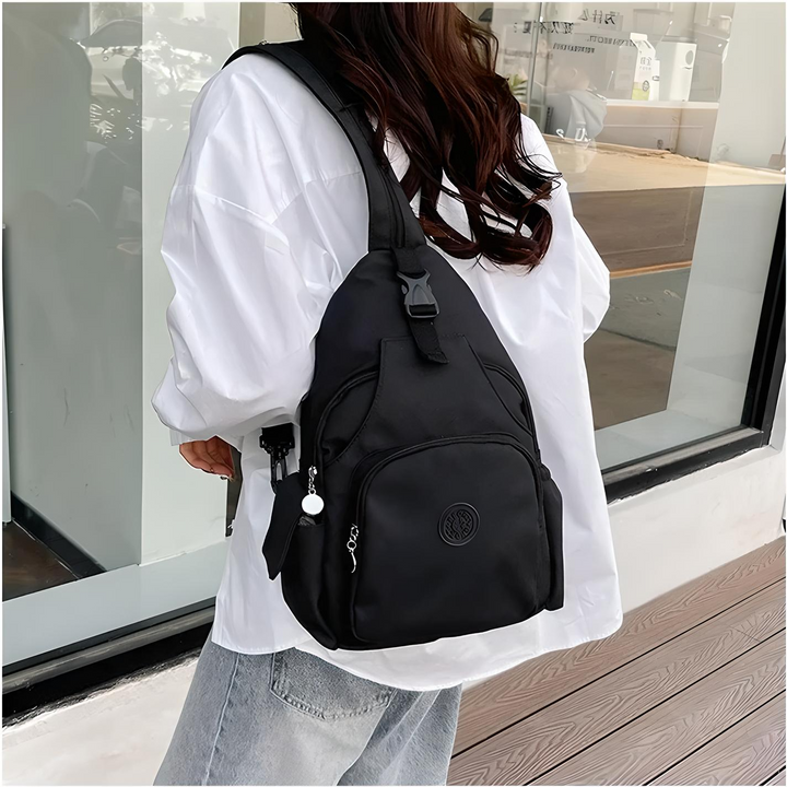 Donna con zaino nero a tracolla, indossa camicia bianca e jeans. Zaino casual, moda urbana, accessorio pratico per viaggi e quotidiano.