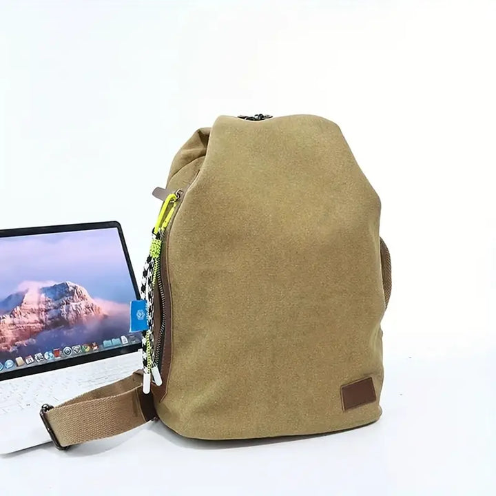 Zaino beige in tessuto con tasca laterale, accanto a un laptop aperto. Design moderno, ideale per scuola o lavoro. Accessori alla moda.