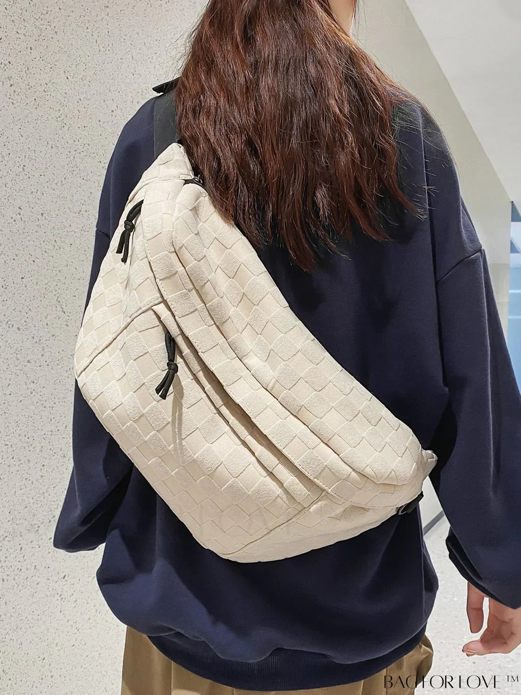 Donna con borsa a tracolla beige intrecciata, indossa maglia blu scuro. Accessorio moda casual, ideale per shopping e viaggi.