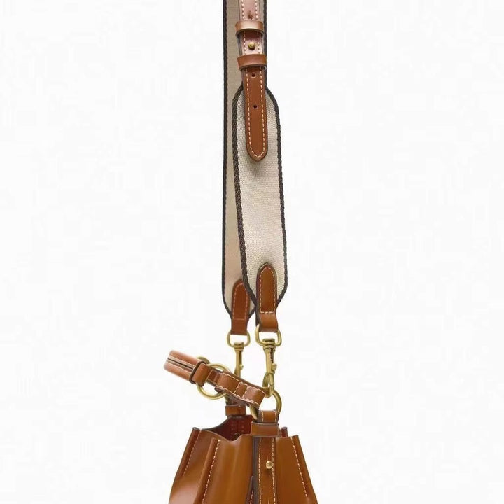 Borsa a secchiello in pelle marrone con tracolla regolabile in tessuto beige, dettagli in metallo dorato. Accessorio moda elegante e versatile.