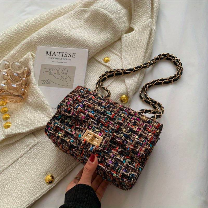 Borsa a tracolla in tweed multicolore su cappotto bianco, con catena dorata e chiusura a scatto. Accessorio moda elegante e chic.