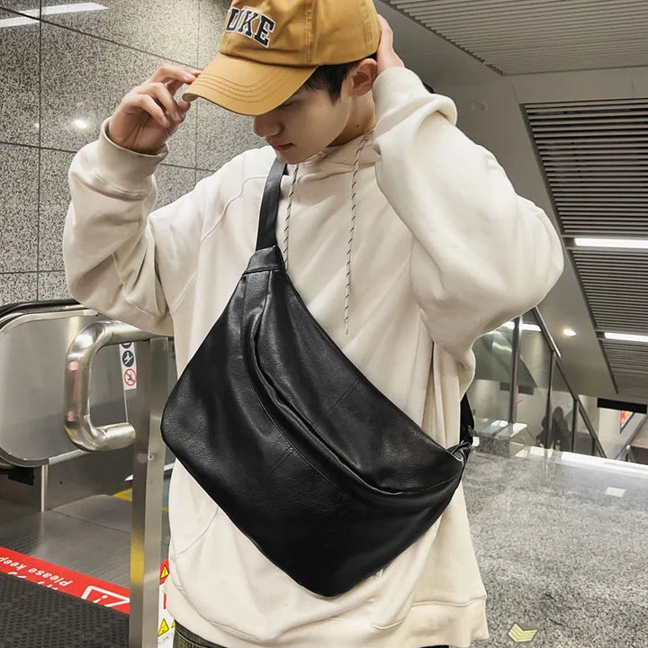 Giovane con felpa bianca e cappello beige indossa una borsa a tracolla nera in pelle in una stazione della metropolitana. Moda urbana, accessori uomo.