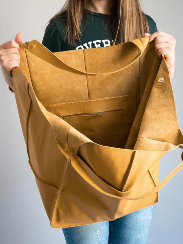 Donna con borsa shopper in pelle marrone chiaro, ampia e aperta, con tasca interna con zip. Accessorio moda, stile casual, capiente e versatile.