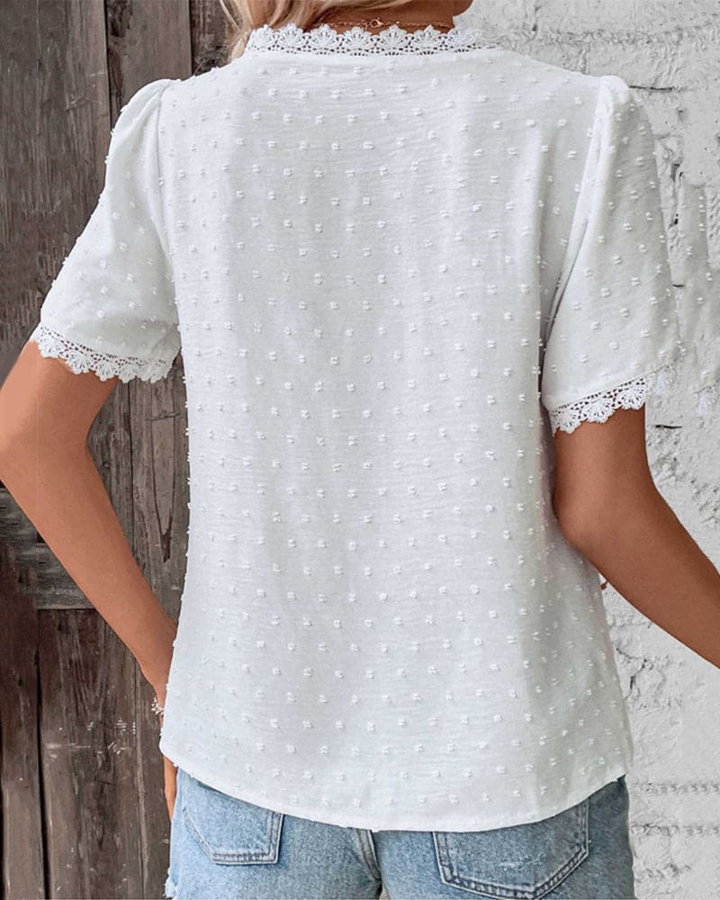 Maglietta bianca a maniche corte con dettagli in pizzo e motivo a pois, indossata da una donna di spalle, abbinata a jeans chiari.