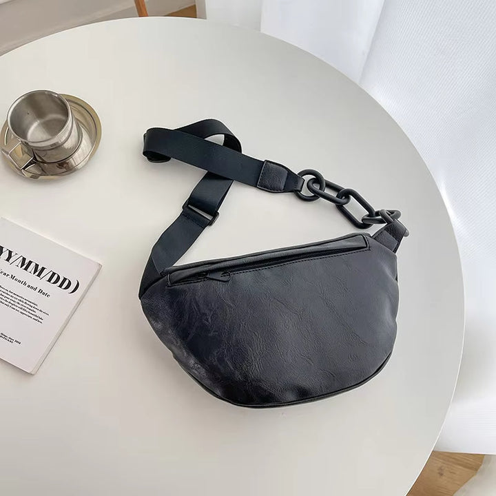 Marsupio nero in pelle su tavolo bianco, con tazza di caffè e rivista. Accessorio moda unisex, stile casual, ideale per viaggi e uso quotidiano.