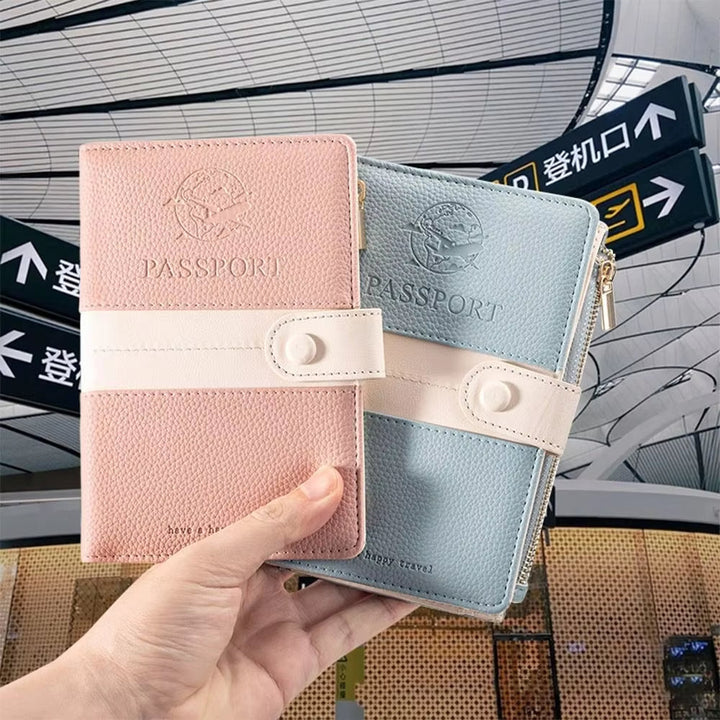 Due portapassaporti in pelle rosa e azzurro con chiusura a bottone, tenuti in mano in un aeroporto moderno. Accessori viaggio eleganti e funzionali.
