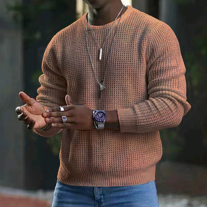 Maglione uomo marrone a maglia grossa, indossato con jeans blu. Accessori: orologio sportivo, collane e anelli. Moda casual autunnale.