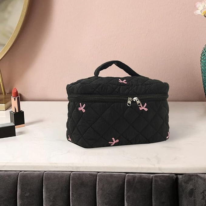 Borsa cosmetica nera trapuntata con cerniera, decorata con fiocchi rosa, su tavolo da trucco. Accessorio elegante per organizzare trucchi.