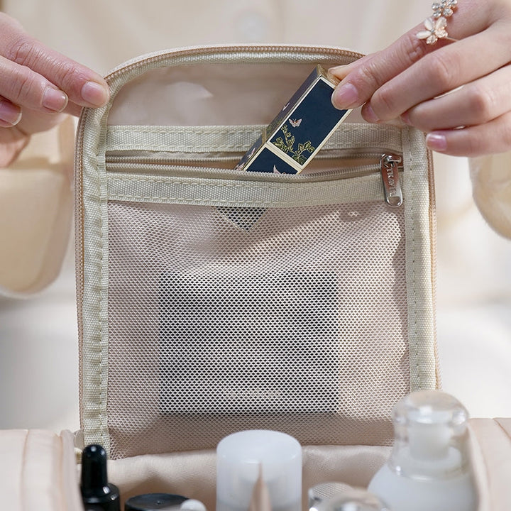 Mani femminili inseriscono un rossetto elegante in una borsa cosmetica beige con tasca a rete. Accessori trucco, organizzazione viaggio, bellezza.