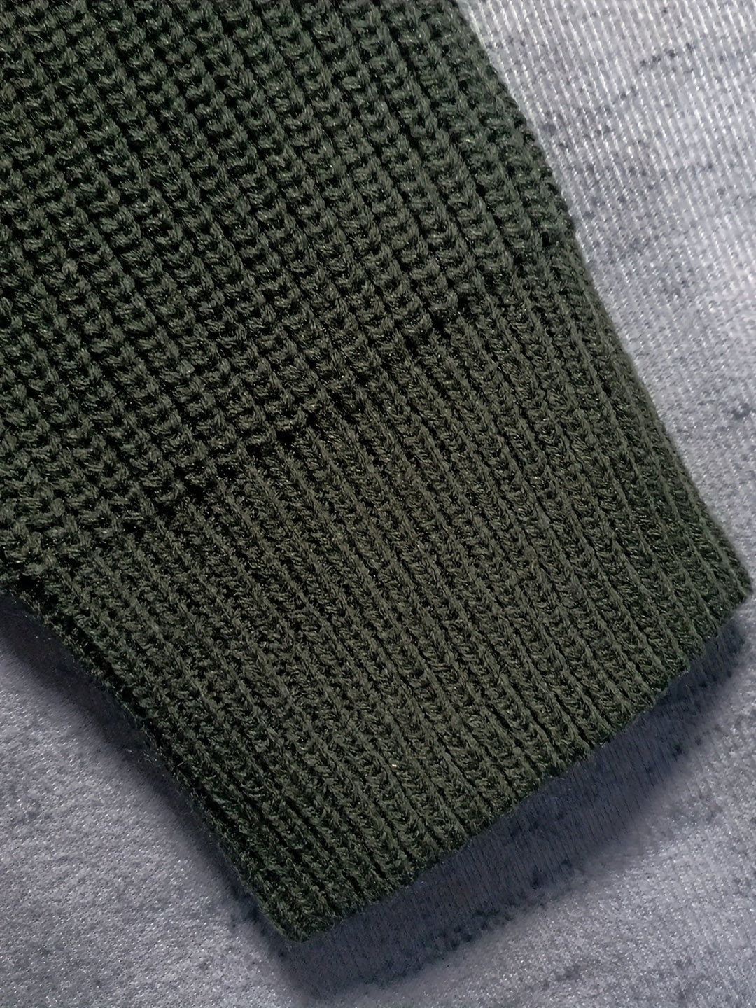Manica maglione verde scuro in maglia a coste su sfondo grigio. Tessuto caldo e morbido, ideale per l'inverno. Moda uomo, abbigliamento casual.