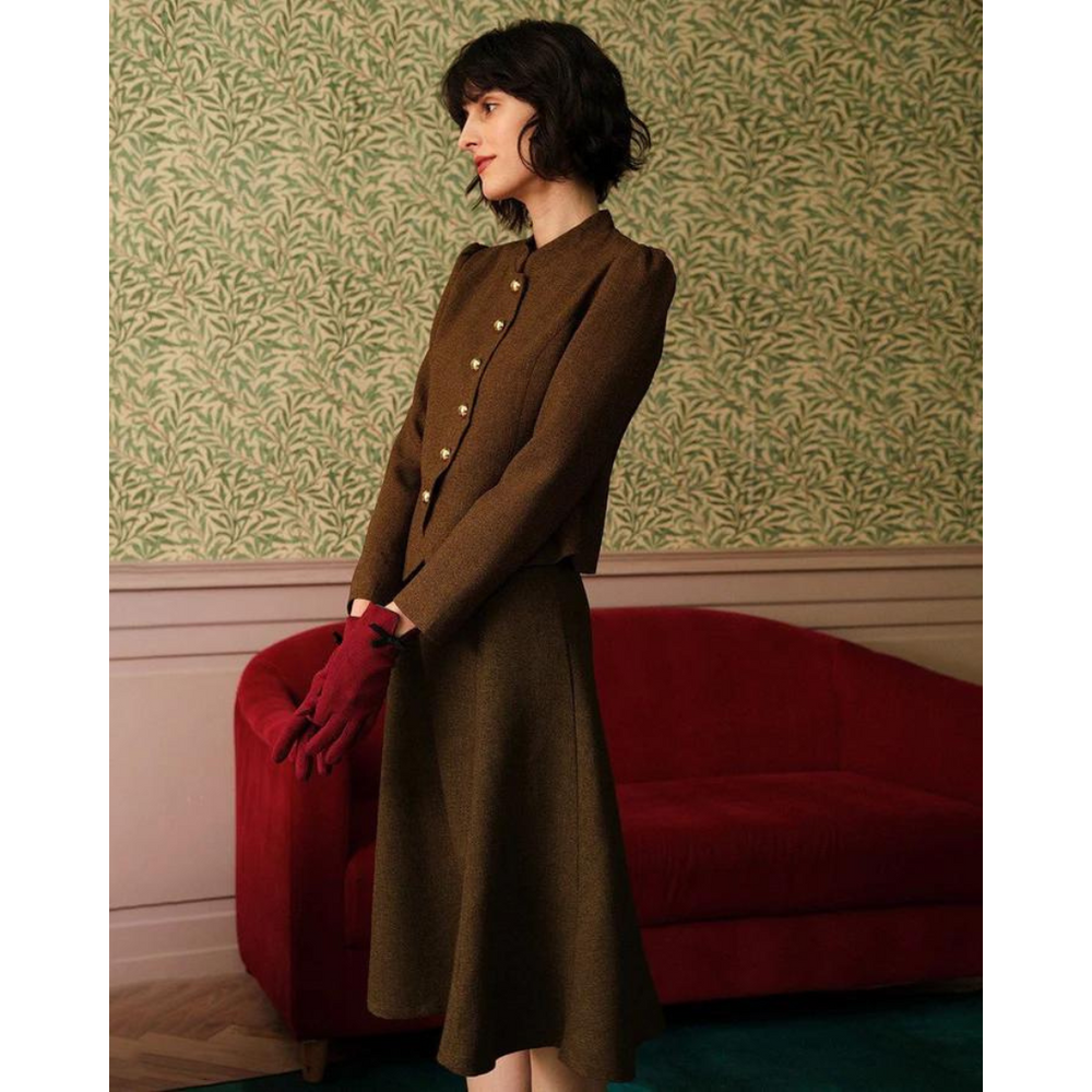Donna con abito marrone vintage, guanti rossi, davanti a divano rosso e parete con carta da parati verde. Moda retrò elegante.