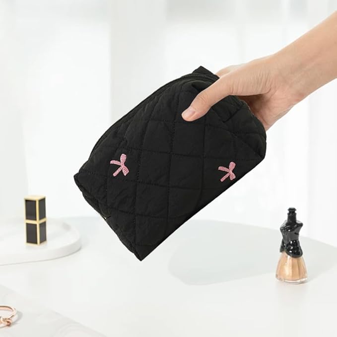 Mano che tiene una pochette nera trapuntata con fiocchi rosa, su tavolo bianco. Accessorio moda donna, elegante e pratico.