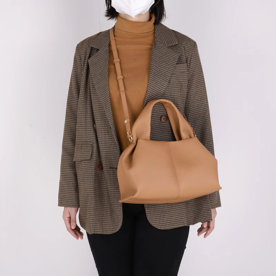 Donna con cappotto a quadri e borsa a mano beige in pelle, elegante e moderna, perfetta per moda autunnale. Accessorio versatile e chic.