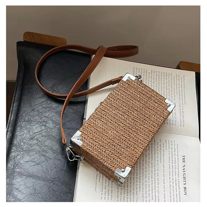 Borsa a tracolla in rattan intrecciato su sedia nera, design rettangolare, dettagli in metallo argentato, stile boho chic, moda donna.