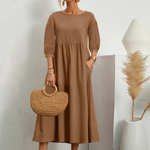 Donna con abito marrone lungo, maniche a tre quarti, borsa in paglia intrecciata, sfondo bianco minimalista, decorazioni naturali.