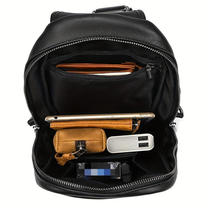 Zaino in pelle nera aperto, mostra tasche interne con smartphone, portafoglio, power bank e chiavi. Accessori organizzati per viaggio e lavoro.
