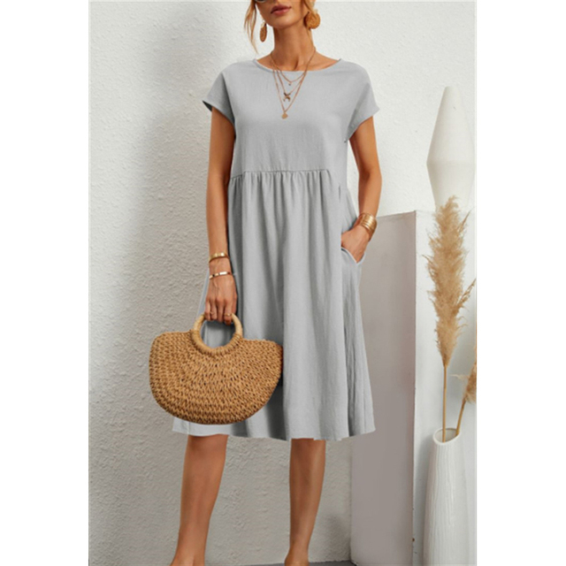 Abito estivo donna grigio chiaro, maniche corte, con tasche. Accessori: borsa paglia, collana oro. Look casual elegante.
