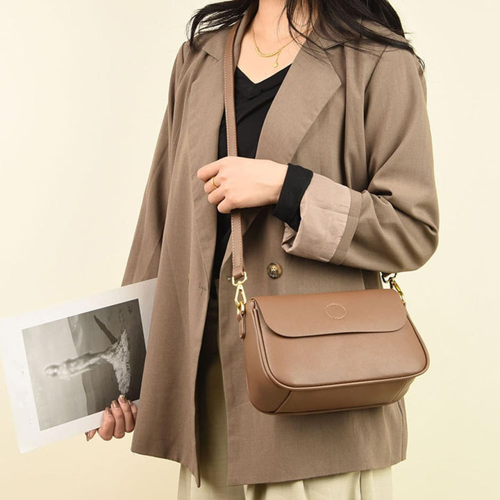 Donna con borsa a tracolla marrone in pelle, indossa blazer beige e tiene una foto. Elegante accessorio moda femminile, stile casual chic.