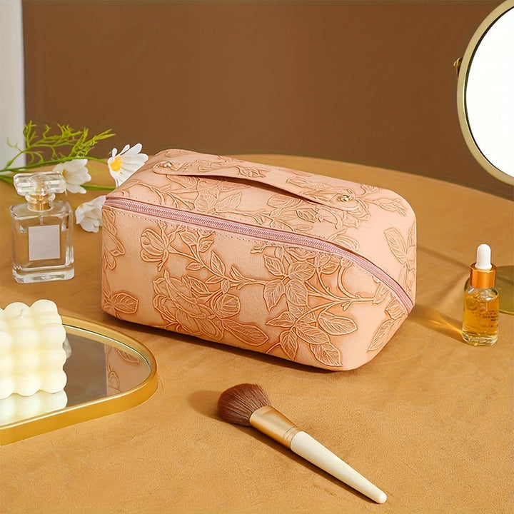 Astuccio trucco beige con motivo floreale, specchio, profumo, pennello e olio essenziale su tavolo. Accessori bellezza eleganti e funzionali.