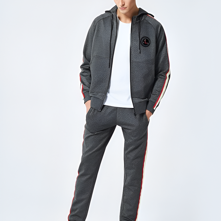 Uomo in tuta sportiva grigia con dettagli rossi e bianchi, giacca con cappuccio e pantaloni coordinati, moda casual maschile moderna.