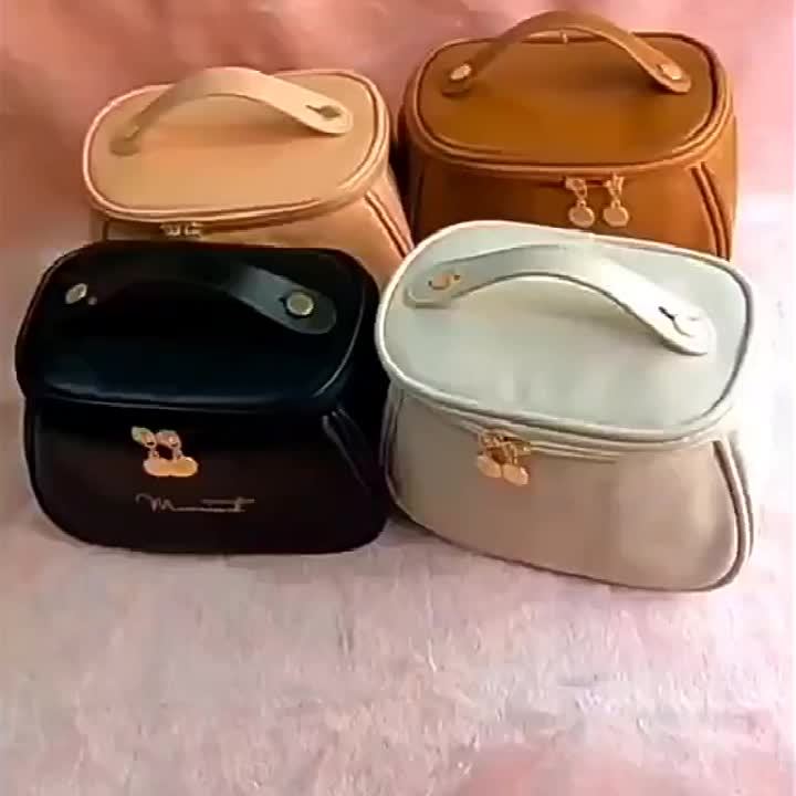 Quattro borse cosmetiche in ecopelle di diversi colori: nero, beige, marrone chiaro e bianco, con chiusura a zip e manico superiore.