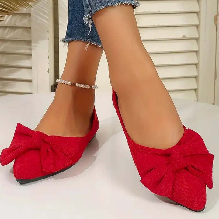 Scarpe ballerine rosse con fiocco, indossate con jeans strappati alla caviglia. Eleganti e alla moda, ideali per look casual e chic.