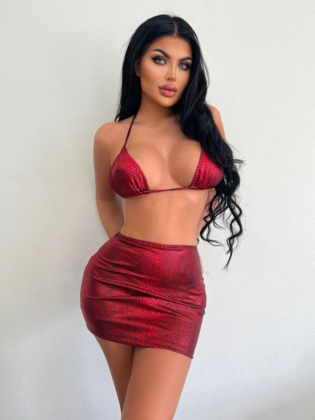Modella in bikini rosso lucido con stampa serpente, posa contro sfondo bianco. Moda estiva, abbigliamento da spiaggia, tendenze 2023.