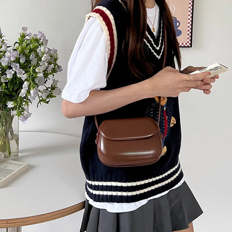 Giovane donna con gilet a righe blu e borsa a tracolla marrone, tiene uno smartphone. Moda casual, outfit autunnale, stile urbano.