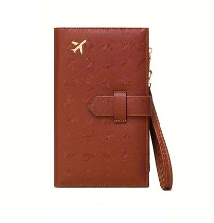 Portafoglio da viaggio in pelle marrone con chiusura a cinghia e icona dorata di aereo, ideale per passaporti e documenti. Accessorio elegante e funzionale.