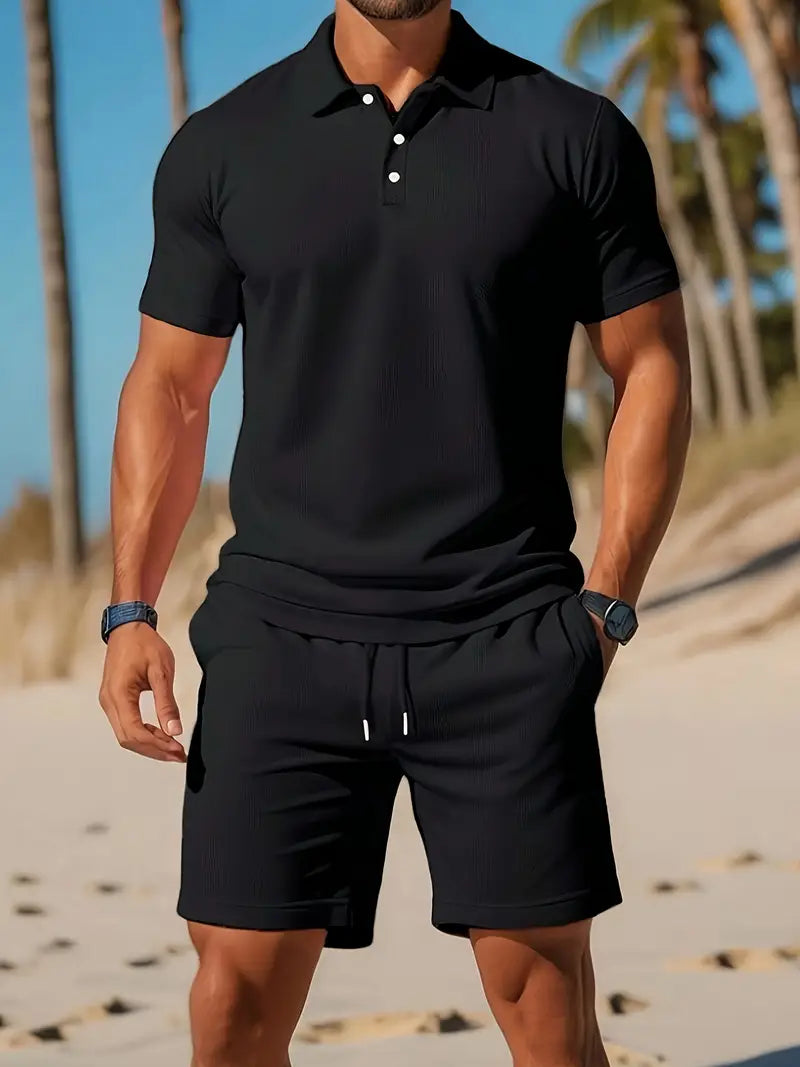 Uomo in spiaggia con polo nera e pantaloncini coordinati, palme sullo sfondo. Moda estiva maschile, abbigliamento casual elegante.