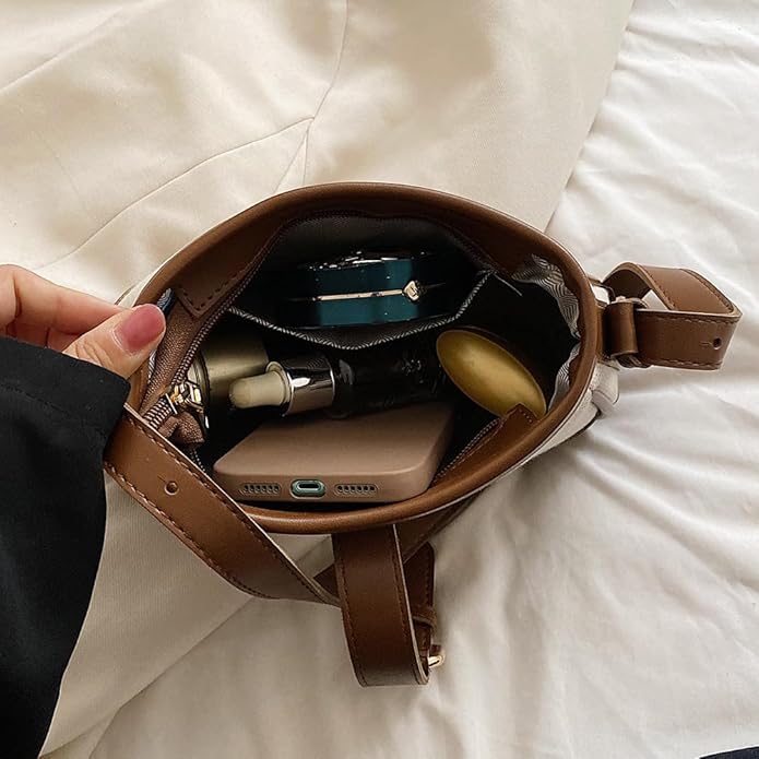 Interno di una borsa a tracolla marrone su letto bianco, contenente smartphone, rossetto, profumo e portafoglio. Accessori moda donna eleganti.