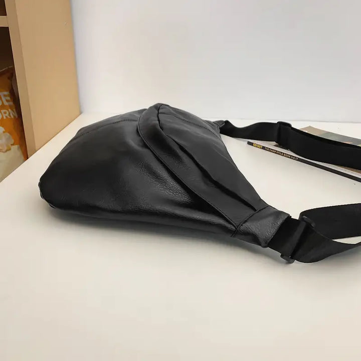 Marsupio in pelle nera su tavolo bianco, design moderno ed elegante, ideale per moda urbana e viaggi. Accessorio versatile e di tendenza.