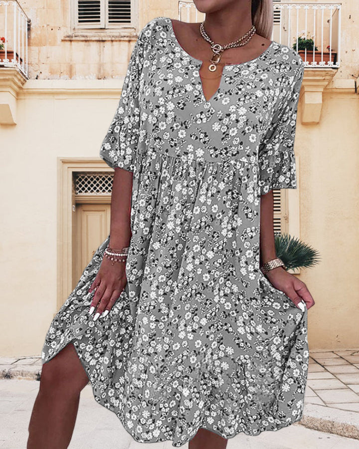 Abito estivo floreale donna, maniche corte, scollo a V, sfondo urbano. Moda casual, elegante, perfetto per giornate calde.