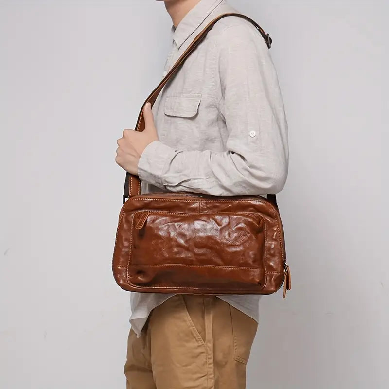 Utente con borsa a tracolla in pelle marrone, design elegante e casual. Ideale per uomo, perfetta per lavoro o viaggio. Accessorio moda versatile.