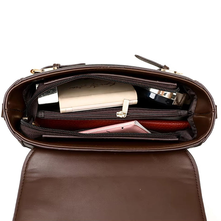 Interno di una borsa a tracolla in pelle marrone con scomparti, contenente un portafoglio, un libro e un rossetto. Accessori moda donna eleganti.