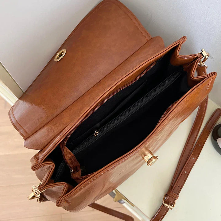 Borsa a tracolla in pelle marrone con chiusura dorata, scomparti interni spaziosi e tracolla regolabile. Elegante accessorio moda donna.