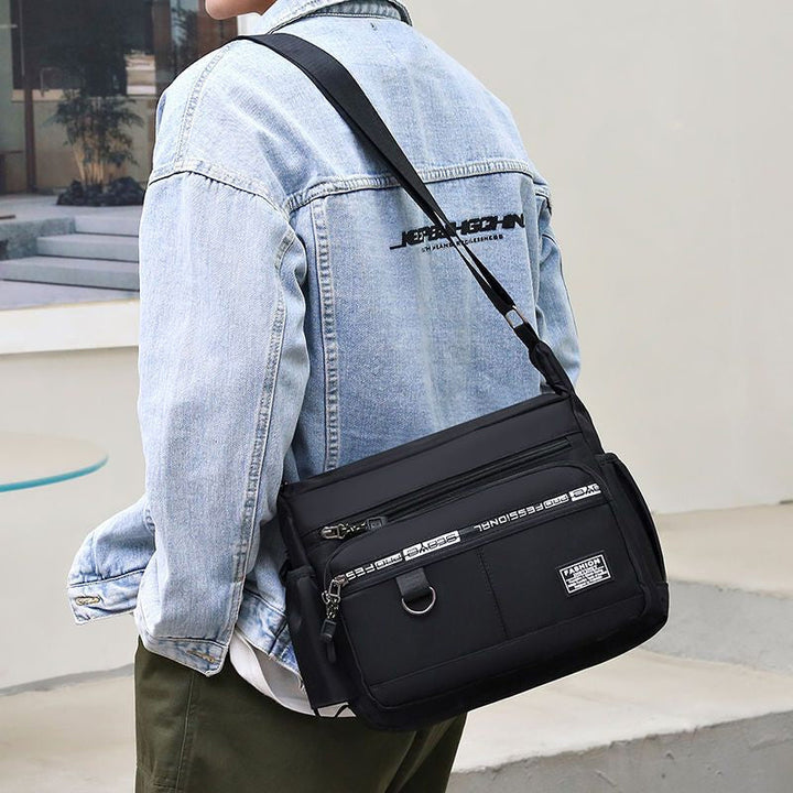 Uomo con giacca di jeans indossa borsa a tracolla nera casual, tasche multiple, stile urbano. Accessorio moda maschile, pratico e versatile.