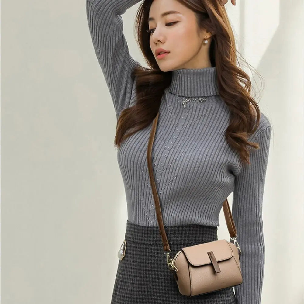 Donna con maglione a collo alto grigio, gonna a quadri e borsa a tracolla beige. Moda autunnale elegante, abbigliamento casual chic.