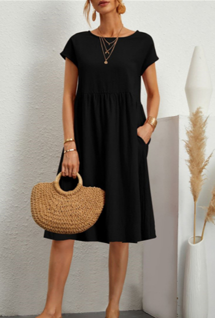 Donna con abito nero casual, borsa di paglia, collane dorate, bracciali. Moda estiva elegante, abbigliamento femminile, accessori trendy.
