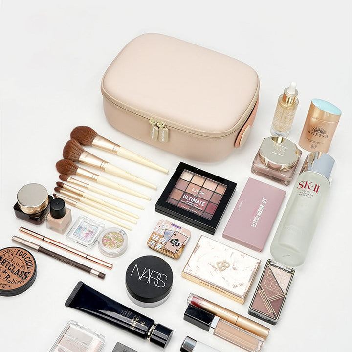 Set di cosmetici e accessori trucco su sfondo bianco, include pennelli, palette ombretti, fondotinta, rossetti e crema SK-II, con borsa beige.
