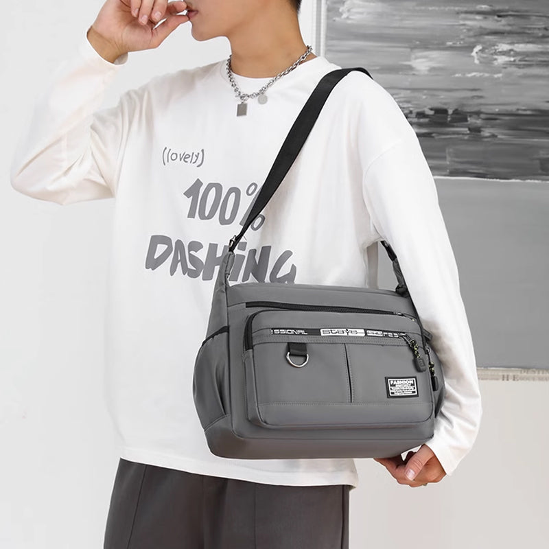 Borsa a tracolla grigia unisex, design moderno, con tasche multiple e cerniere, indossata da persona con maglia bianca. Accessorio moda casual.