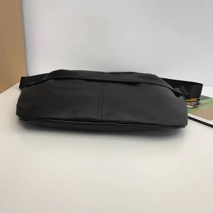Borsa a tracolla in pelle nera su sfondo bianco, design elegante e moderno, ideale per uomo e donna, accessorio moda versatile e pratico.