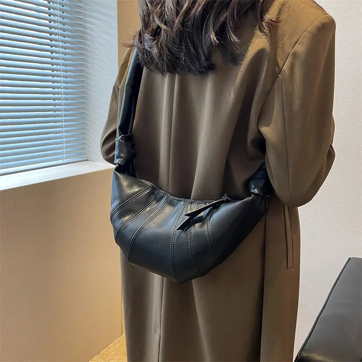 Donna con cappotto marrone indossa borsa a tracolla in pelle nera, design moderno, elegante e versatile, perfetta per moda autunno inverno.