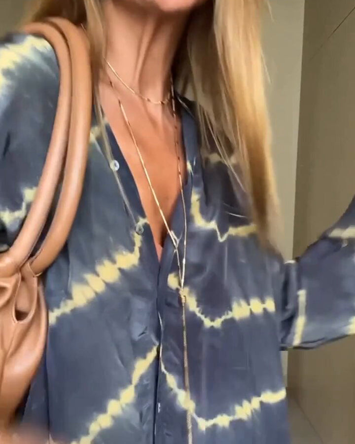 Donna con camicia tie-dye blu e gialla, collane dorate e borsa marrone. Moda casual, stile boho-chic, tendenze abbigliamento femminile.