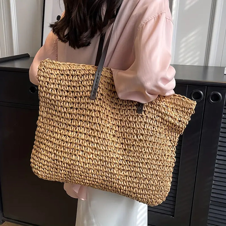 Donna con borsa a tracolla in paglia intrecciata, stile casual, manici in pelle marrone, perfetta per l'estate e lo shopping.