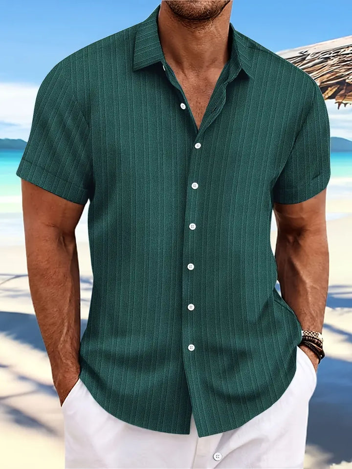 Camicia estiva da uomo verde a righe, maniche corte, sfondo spiaggia. Ideale per moda mare, look casual elegante.