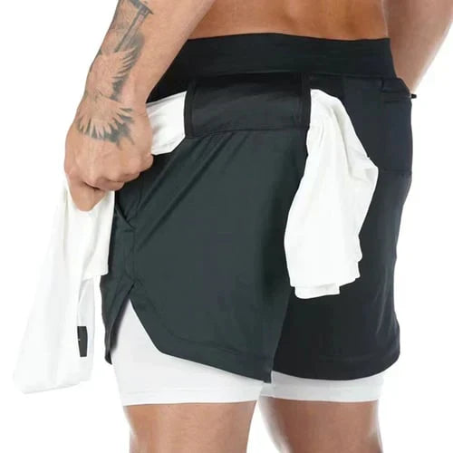 Uomo in pantaloncini sportivi neri con tasca, tiene una maglietta bianca. Abbigliamento fitness, moda uomo, pantaloncini da corsa.