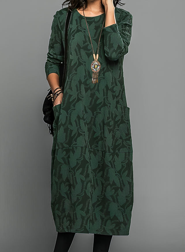 Abito lungo verde con motivo floreale, maniche lunghe, tasche frontali, collana pendente. Elegante e casual, perfetto per l'autunno.