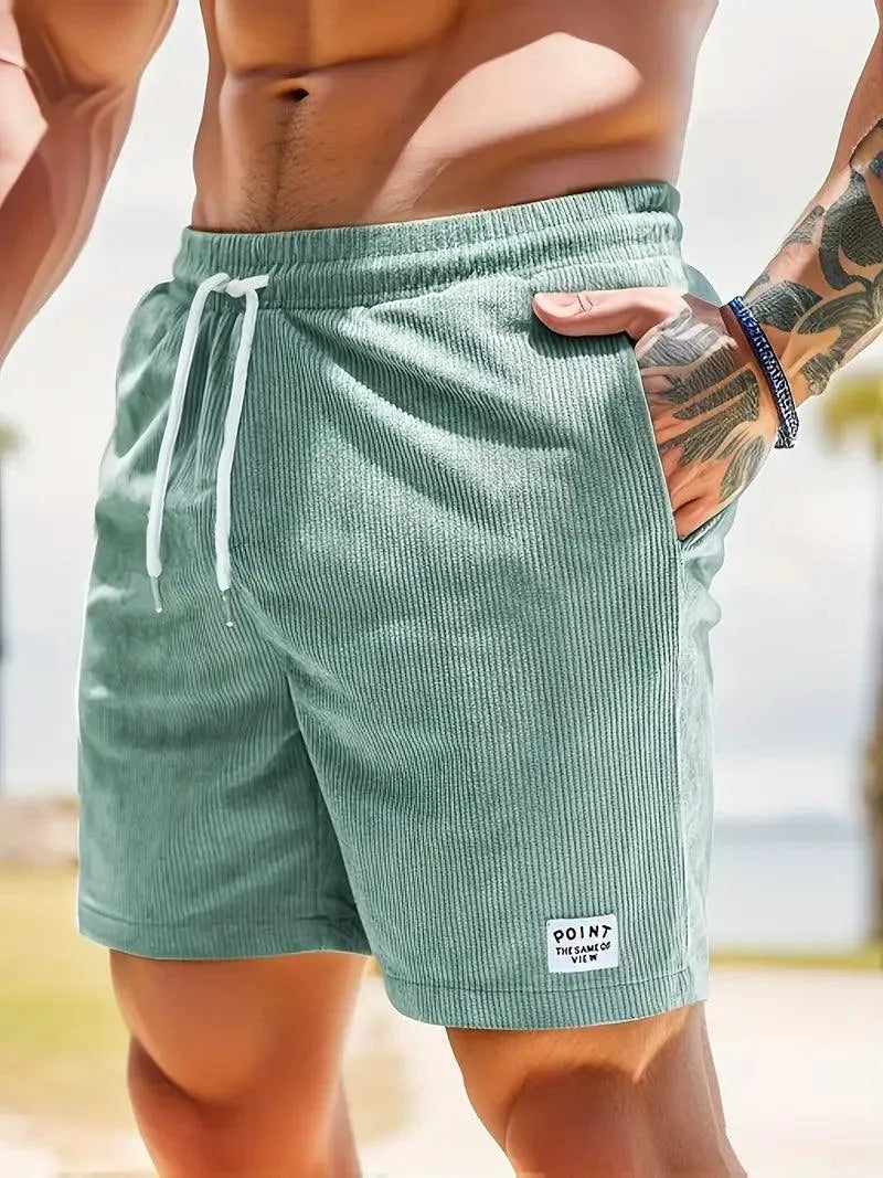 Uomo in costume da bagno verde menta a righe, con cordoncino bianco, in spiaggia. Moda estiva, abbigliamento mare, stile casual.